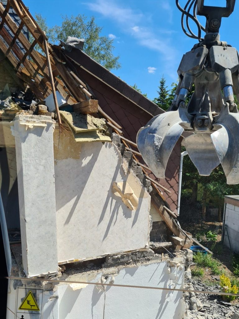 Abgerissene Gebäudewände mit zweigeteiltem Greifarm im Hintergrund.